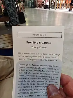 Person holding a printed French booklet titled “Première cigarette” while seated in a public indoor area