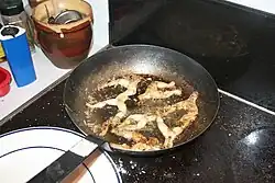 Frog legs frying in oil in a black pan on a kitchen stove in France.