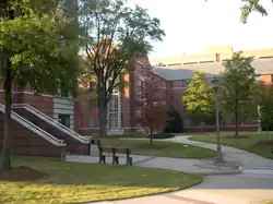 A red brick and white concrete, four-story apartment building with a landscaped courtyard in the foreground