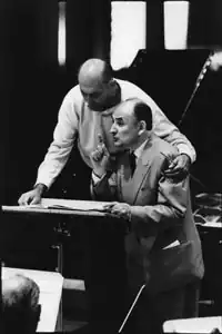 two men, both bald, one standing and one sitting