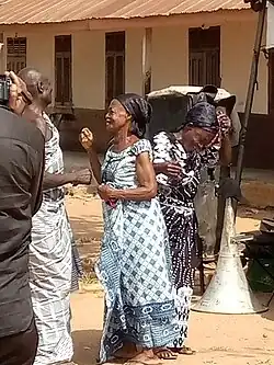 two African women in patterned dresses and head scarfs crying at a funeral
