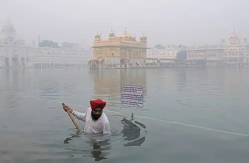 A Sikh pilgrim at the Harmandir Sahib—the Golden Temple—in Amritsar, Punjab, performing seva, or volunteer work, by helping clean the sacred pond