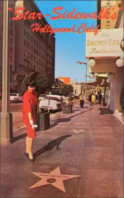 A woman in a red dress points at Charlton Heston's star with other stars, Hollywood Brown Derby, Vine Street, and the Dyas Building viewable behind it. The text "Star-Sidewalks / Hollywood, Calif. printed in a red cursive font at the top of the image