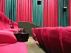 Interior of Hoyts Cinemas auditorium in Perth, Australia, with stadium seating with cup holders, acoustic wall-hangings and wall-mounted speakers.