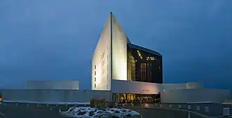 The John F. Kennedy Library, a white triangular tower, rises beside a black glass building, with circular structures on either side.