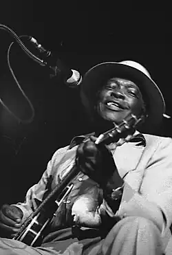Close up image of John Lee Hooker performing with his guitar on stage while smiling, taken in 1978.