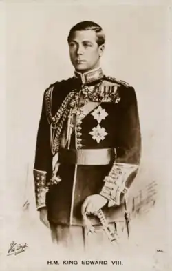A portrait of George VI in purple coronation robes and holding the sceptre in his right hand. He is facing slightly rightwards, and towards the table to his right that holds the Imperial State Crown.