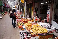 A female customer browsing a fruit shop. Banana and grapes are displayed on the front.