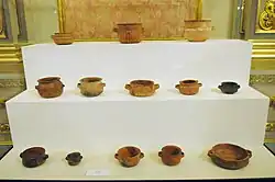 Ancient clay pots of different shapes and sizes displayed on white stepped stands.