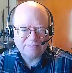 A bespectacled balding man in a chequered shirt facing the camera.