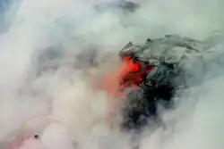 Photo showing clouds of steam surrounding lava that is partly black and partly glowing orange