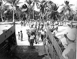 A black and white photo of several people boarding a ship carrying their belongings.