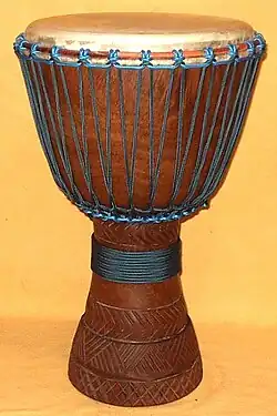 Brown goblet-shaped wood and leather drum with blue rope on an alabaster background