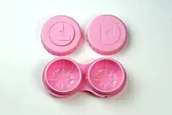 An open lens care. The lens caps are engraved with the letters L and R to indicate left and right. The case body is shaped as a pair of glasses and contains two holes for the lenses.