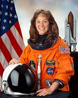 A smiling brunette white woman in her orange space suit