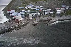 A village of 40–50 mostly small buildings built on a steep, rocky coastline; some structures higher on the hill are built on stilts