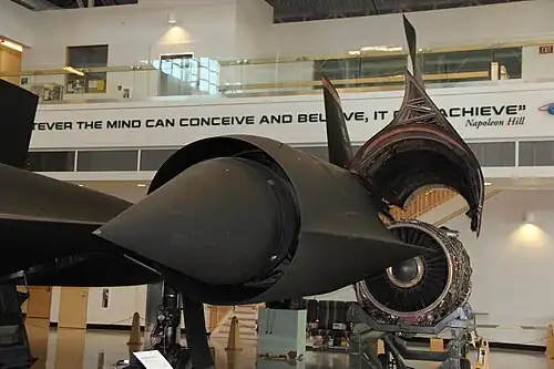 Entry to the inlet. Behind is the outer wing and hinged portion of the nacelle that encloses the engine. The spike is shown in the forward position (for speeds below Mach 1.6). Just discernible behind the cowl lip are spike boundary layer bleed slots where the normal shock is located at higher speeds when the spike has moved rearwards, the cowl bleed "shock trap" ram intake, streamlined bodies ("mice") and, between the mice, the forward bypass door openings[77] that dump unwanted air externally through the front louvers and cause nacelle drag.[78] When the landing gear is down, ambient air flows in reverse through the bypass to supplement the front inlet flow into the engine.