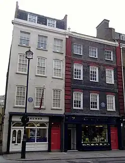 A color photograph of two adjacent buildings, the one on the left is white and the on the right is dark brown.