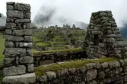 Stone ruins with moss-covered walls and terraces, and misty mountain backdrop.