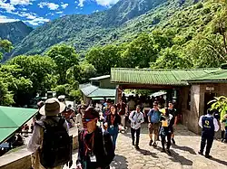 A group of tourists walking through the main entrance with mountains and greenery in the background.