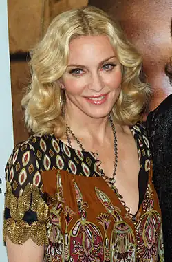 Madonna wearing a loose dress with black and brown prints on it. She is looking to the right and smiling.