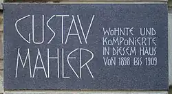 A dark plaque with white lettering in which the composer's name is shown in extra large characters on the left, the main message in smaller characters on the right