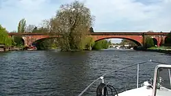 a red brick built bridge with shallow arches spanning a river, viewed from the front of a small boat