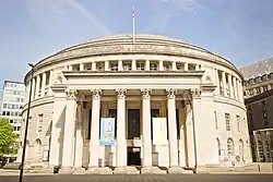 A neopalladian grand stucco building as viewed from directly in front, with a portico extending from it. The building itself is a cylindrical shape and the photo sets it against a blue sky.