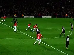 A wide shot of a football match with Manchester United in red in possession against Lyon in black.