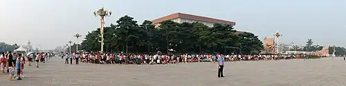 A large mausoleum in the middle of a public square, surrounded by a long line of people, as they wait to enter