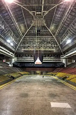 The interior of an arena. There are bands of seats of different colours, and there is a high, vaulted ceiling.