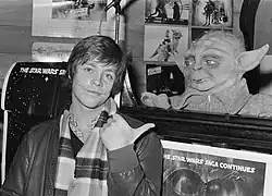 A photograph of Mark Hamill in 1980, promoting The Empire Strikes Back while pointing at a puppet of Yoda