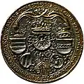 A gold-and-silver coin featuring five coats of arms, three crowned, and the chain of the Order of the Golden Fleece. The coin is surrounded by text.
