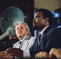 Michael Somare sitting at a desk speaking with an out of focus microphone in front of the shot