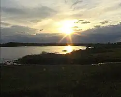 The sun low over the horizon over a body of water surrounded by dark vegetation