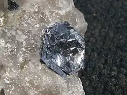 Lustrous, silvery, flat, hexagonal crystals in roughly parallel layers sit flowerlike on a rough, translucent crystalline piece of quartz.