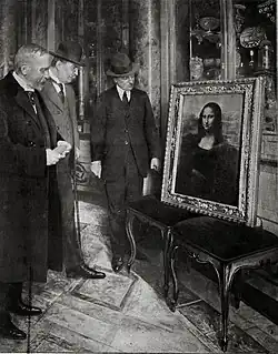 Three men in suits and hats stand examining the framed Mona Lisa painting displayed on two benches in an ornate room