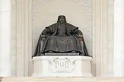 A statue of a seated man, placed on an inscribed plinth.