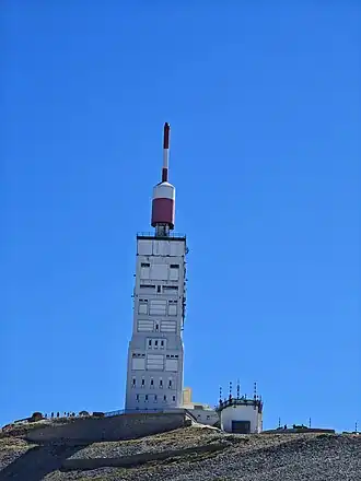 The white and red summit communications tower on Mont Ventoux rising above a rocky peak under a clear blue sky