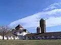 Two wings of a white barn with two silos under a blue sky with cirrus clouds