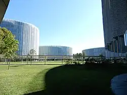 View of the new SDA Bocconi campus in Milan. On the foreground, a green area can be seen. In the background, two white-cladded, circular-shaped buildings can be seen.
