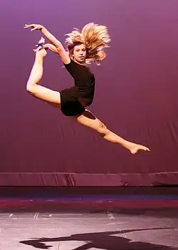 A contemporary dancer performs a single leg stag leap or firebird.