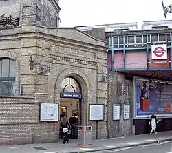 A beige-bricked building with a rectangular, dark blue sign reading "PARSONS GREEN" in white letters all under a light blue sky with white clouds