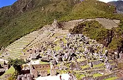 Panoramic view of an Inca quarry with terraces and a pile of large, irregular granite blocks.