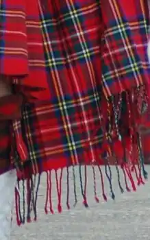 Zoom-in on a predominantly red tartan plaid, showing its bottom edge with a purled fringe