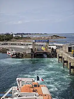 View of the Port of Roscoff showing the ferry ramp, harbor structures and a vessel departing toward open water.