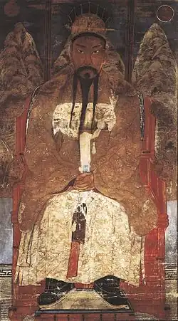 Asian man with mustache and gold robes, sitting down.