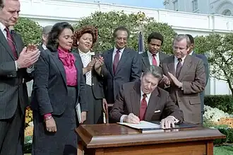 Ronald Reagan at the signing ceremony for Martin Luther King Jr. Day legislation in the Rose Garden. Coretta Scott King, George H. W. Bush, Howard Baker, Bob Dole, Jack Kemp, Samuel Pierce, and Katie Hall looking on.