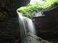 A waterfall pours through a semicircular hole in a rock ledge