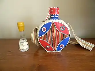 A small bottle of clear liquid and an ornate leather flask sitting on a table